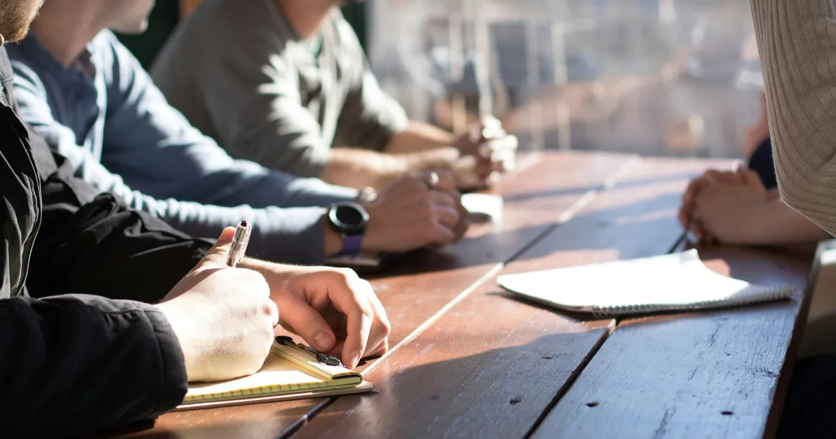 A picture of people working together at a conference table with notepads.